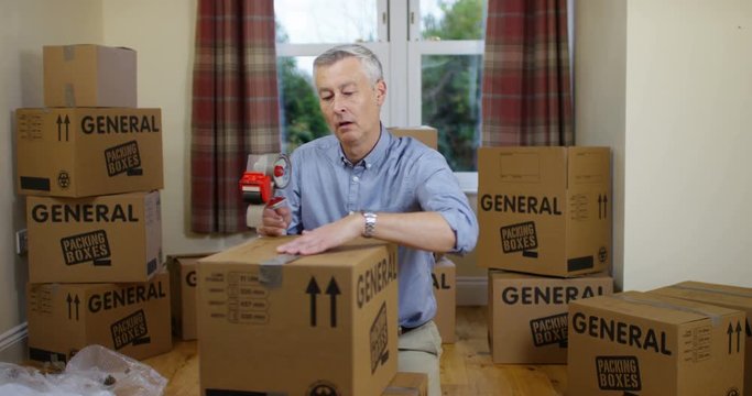4K Fed up man packing boxes for house move, looking at camera with sad expression. Slow motion.