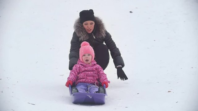 Mom rolling her little daughter on a sled in a winter park