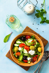 Greek salad with fresh vegetables, feta cheese and black olives on a blue stone or concrete table. Diet, concept of vegetarian food. Copy space, top view flat lay background.