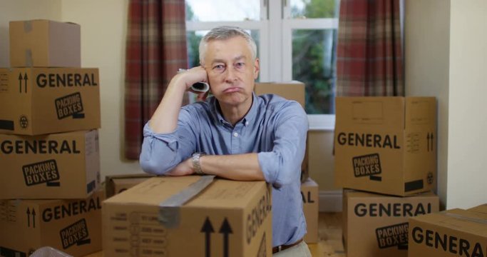 4K Mature man packing boxes for house move, staring at camera with fed up expression. Slow motion.