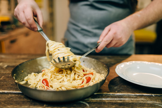 Chef cooking pasta, pan on wooden kitchen table