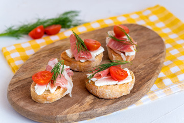 Italian prosciutto and feta cheese bruschetta decorated by tomato and dill. Antipasti on grilled baguette bread.