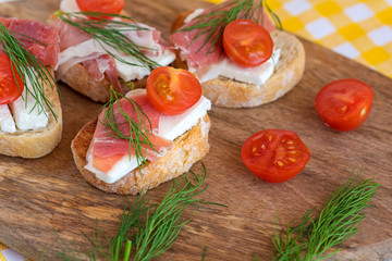 Italian prosciutto and feta cheese bruschetta decorated by tomato and dill. Antipasti on grilled baguette bread.