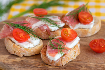 Italian prosciutto and feta cheese bruschetta decorated by tomato and dill. Antipasti on grilled baguette bread.