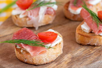 Italian prosciutto and feta cheese bruschetta decorated by tomato and dill. Antipasti on grilled baguette bread.