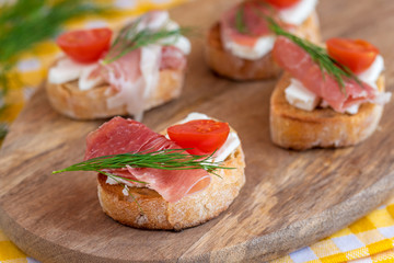 Italian prosciutto and feta cheese bruschetta decorated by tomato and dill. Antipasti on grilled baguette bread.