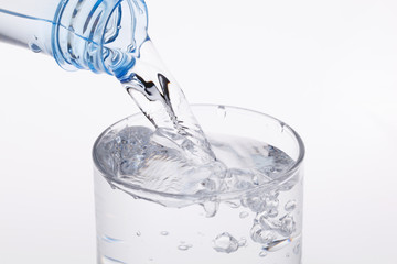 Pouring water from bottle into glass on white background.