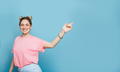 Look over there. modern young woman, pointing copy space and looking at camera while standing against blue pastel background