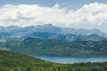 Fototapeta na wymiar Sunny day mountain lake and blue cloudy sky scenic landscape background.