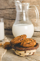 Oatmeal chocolate chip cookies, jug and glass of milk, rustic wooden background.