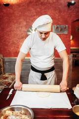 Male chef roll out the dough with a rolling pin