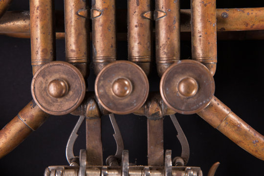 Vintage bronze pipes, valve, key mechanical elements french horn, black background. Good pattern, prompt music instrument.
