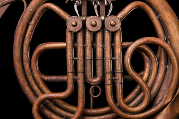 Vintage bronze pipes, valve, key mechanical elements french horn, black background. Good pattern, prompt music instrument.