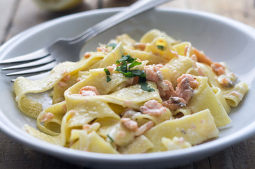 Homemade italian pasta with smoked salmone and creamy sauce and parsley on the top, white plate on the wooden rustic table