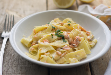 Homemade italian pasta with smoked salmone and creamy sauce and parsley on the top, white plate on the wooden rustic table