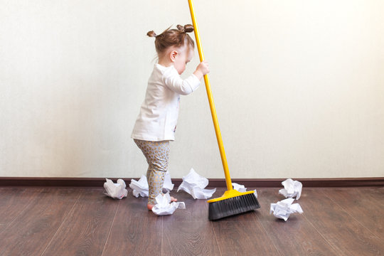 child sweeps broom with paper bins in the apartment, household chores