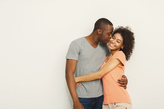 Smiling black couple embracing at white studio