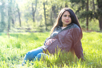 Portrait of a pregnant woman is sitting on a meadow