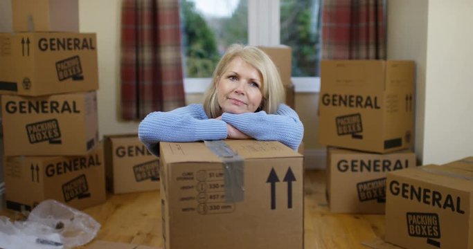 4K Woman surrounded by boxes in new home, looking tired & unhappy