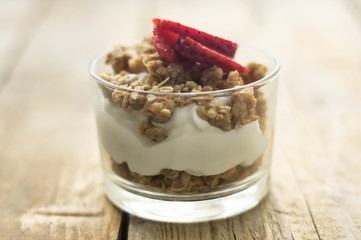Little glass bowl of homemade granola with greek yoghurt and strawberries, isolated on the wooden rustic table