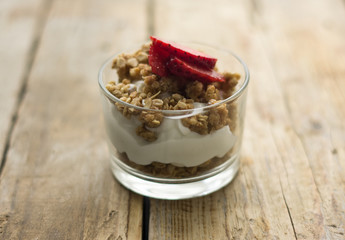 Little glass bowl of homemade granola with greek yoghurt and strawberries, isolated on the wooden rustic table