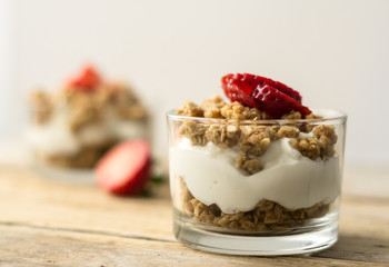 Little glass bowl of homemade granola with greek yoghurt and strawberries, isolated on the wooden rustic table