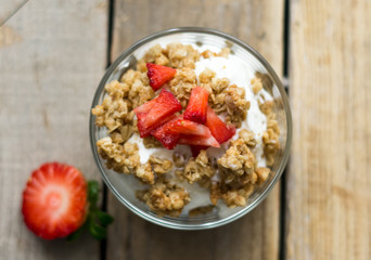 Little glass bowl of homemade granola with greek yoghurt and strawberries, isolated on the wooden rustic table. Flat lay.