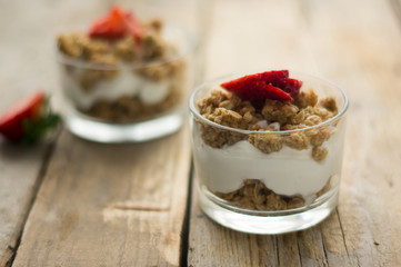 Little glass bowl of homemade granola with greek yoghurt and strawberries, isolated on the wooden rustic table. Flat lay.