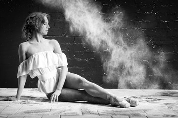beautiful ballet dancer in white clothes sitting on the floor on Pointe in a cloud of dust