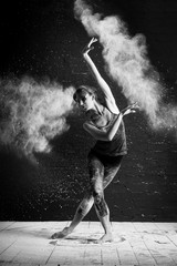 beautiful ballet dancer dancing barefoot on black background in a cloud of dust