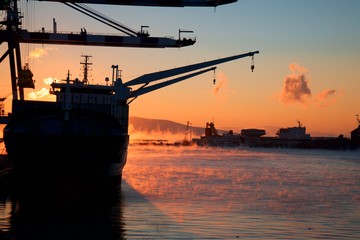 Sunrise over sea port. Steam on the water. Winter season.