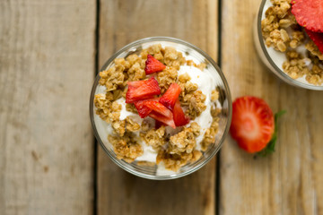 Little glass bowl of homemade granola with greek yoghurt and strawberries, isolated on the wooden rustic table. Flat lay.