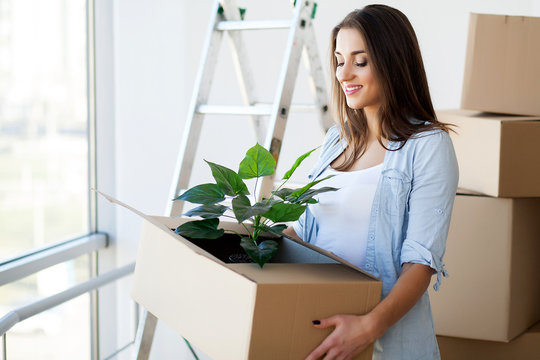 Happy Young Adult Woman Holding Moving Boxes In Empty Room In A New House.