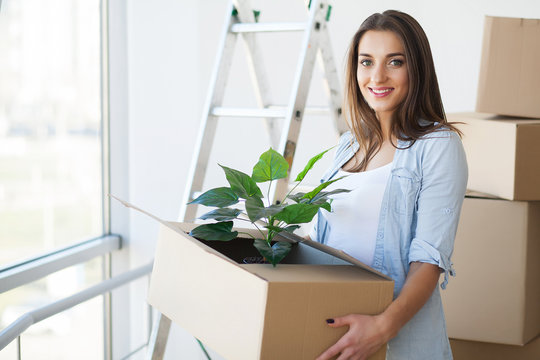 Happy Young Adult Woman Holding Moving Boxes In Empty Room In A New House.