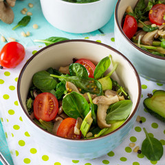 Green vegetarian breakfast in a bowl of avocado, mushrooms, cherry tomato, pine nuts, spinach and dressing with vinaigrette sauce on a wooden table in a rustic style. Diet, concept of vegetarian food.