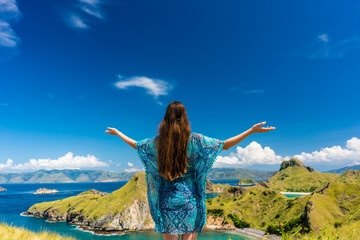 Rear view of a happy tourist enjoying the breeze while standing with outstretched arms outdoors during summer vacation in Padar Island, Indonesia