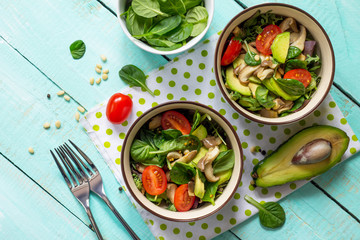 Healthy vegetarian lunch bowl. Avocado, mushrooms, cherry tomatoes, pine nuts, spinach and dressing with vinaigrette sauce on a wooden table in a rustic style. Top view.