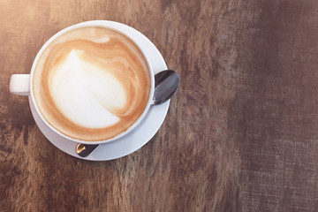 Top view of a white cup with coffee on a wooden background illuminated by sun.