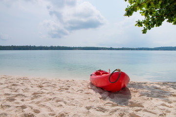 A red kayak on the beach with tropical sea