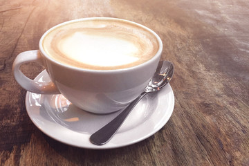 White cup with coffee on a wooden background illuminated by sun.