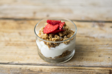 Little glass bowl of homemade granola with greek yoghurt and strawberries, isolated on the wooden rustic table