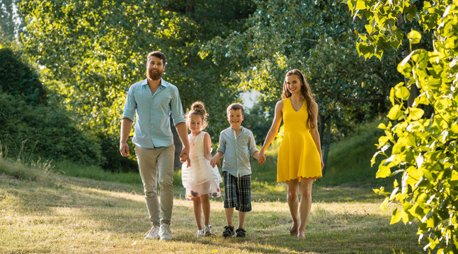 Full length view of a happy family with two children wearing casual summer clothes while holding hands during recreational walk in the park