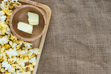 popcorn on wooden plate with butter in wooden bowl on gunny sack cloth, top view, with copy space