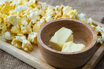 butter in wooden bowl with popcorn on wooden plate on gunny sack cloth