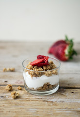 Little glass bowl of homemade granola with greek yoghurt and strawberries, isolated on the wooden rustic table