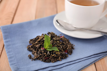 Dry green tea leaves and cup of aromatic beverage on table