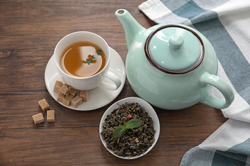 Dry green tea leaves and cup of aromatic beverage on table