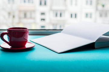 red cup of coffee and a book on a blue background by the window. concept home vacations