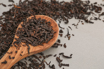 Spoon with dry black tea leaves on grey background