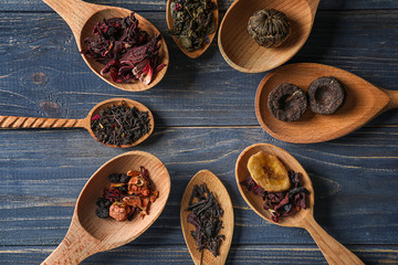 Spoons with different types of dry tea leaves on wooden background